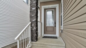 A front view of a house with a beige exterior, a front door, and a stone pillar. - 4 Bedrooms, 3 washrooms, and 2 living rooms, Luxury Home Close to Amenities (Leduc)
