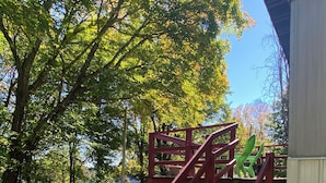 Eine Holztreppe mit roter Handlauf, die zu einem überdachten Bereich führt, umgeben von Bäumen und einem Weg.