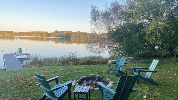 Ein Sitzbereich im Freien am Seeufer mit Adirondack-Stühlen und einem kleinen Feuereimer.