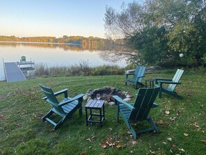 Un espacio al aire libre junto al lago con sillas Adirondack y un pequeño hogar para fuego.