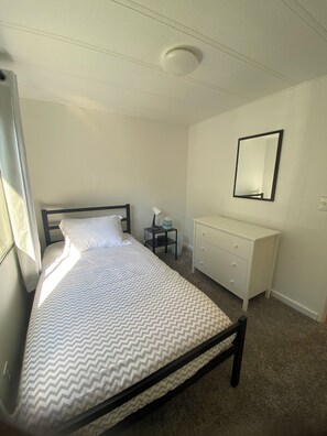 Un dormitorio con cama, cómoda, mesita de noche y espejo en la pared.