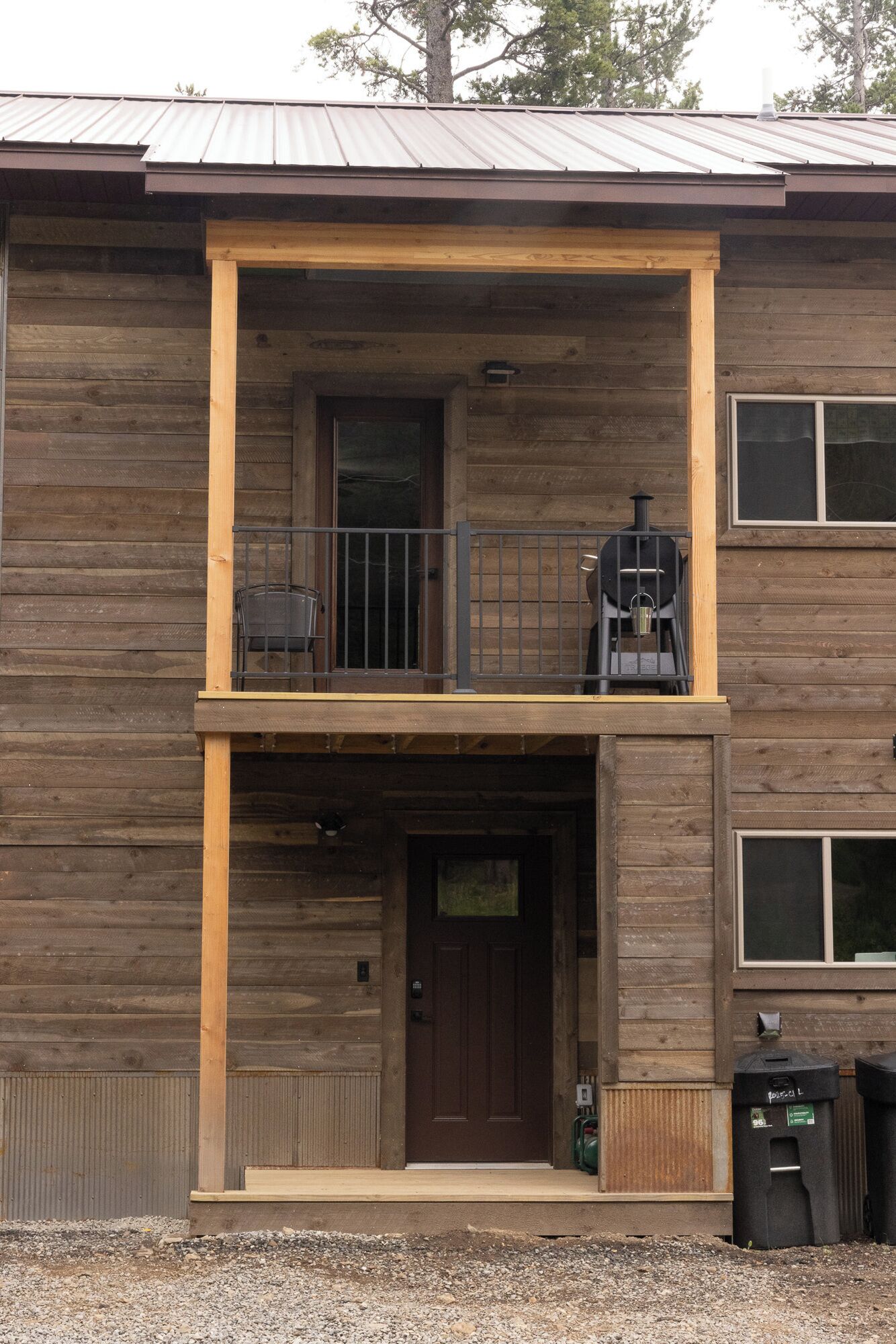 A two-story wooden building with a front door, a balcony with a grill, and a chimney.
