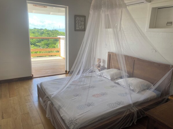Un dormitorio con una cama cubierta por una mosquitera, piso de madera y vistas al verdor a través de una puerta abierta.