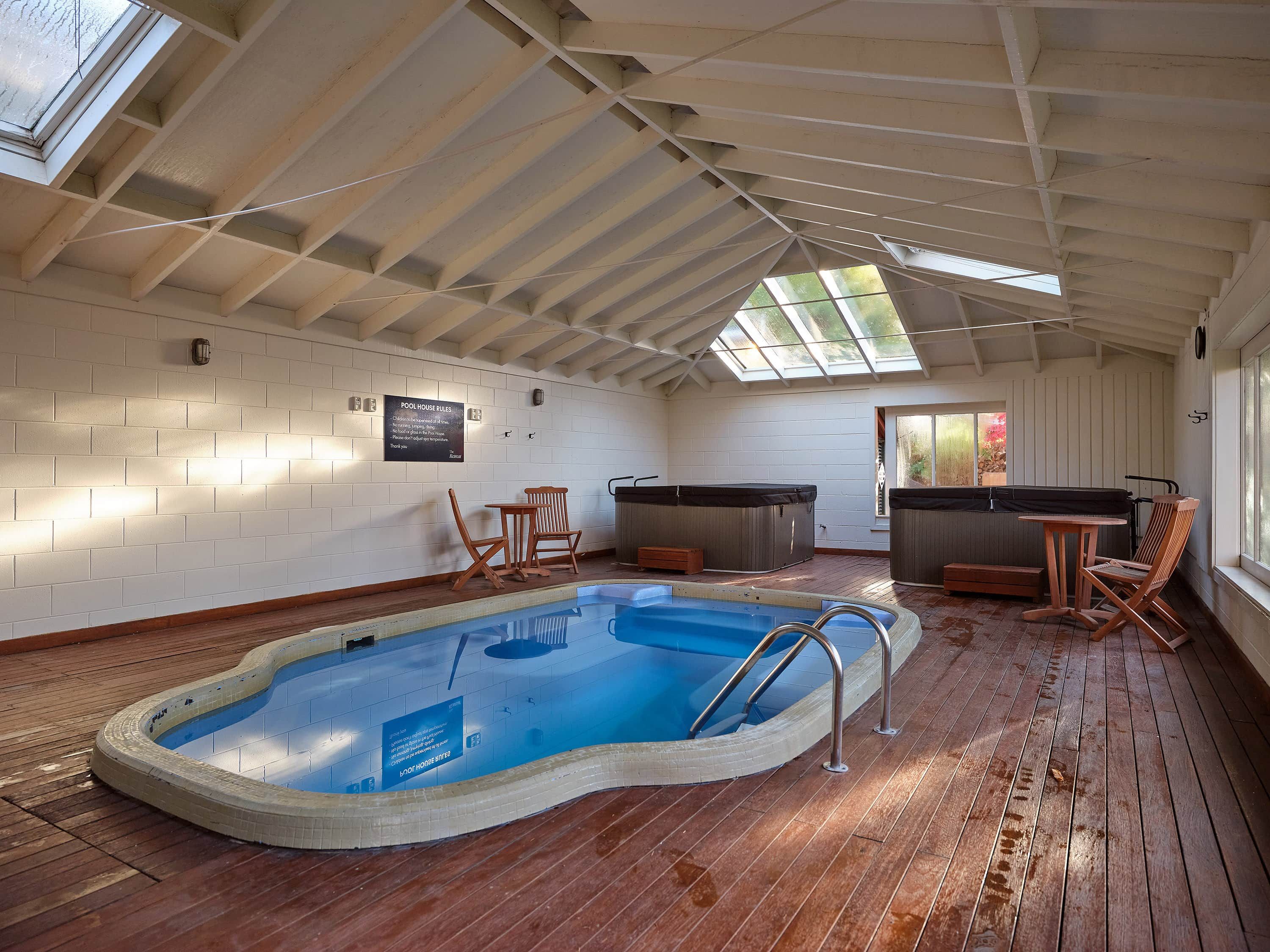 An indoor swimming pool with a wooden deck, a hot tub, and seating areas.