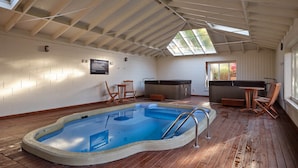 Una piscina interior con terraza de madera, un jacuzzi y zonas de estar.