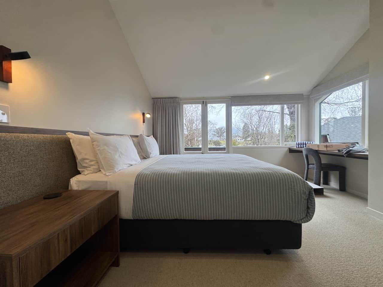 A modern bedroom with a large bed, a wooden bench, a desk, and a chair.
