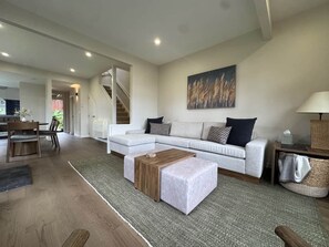 A modern living room with a sectional sofa, a wooden coffee table, and a dining area with chairs. - Chalet 7 - The Retreat (Taupo)