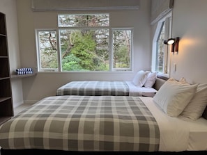 Quarto com duas camas, janela com vista para árvores e luminária fixada na parede.