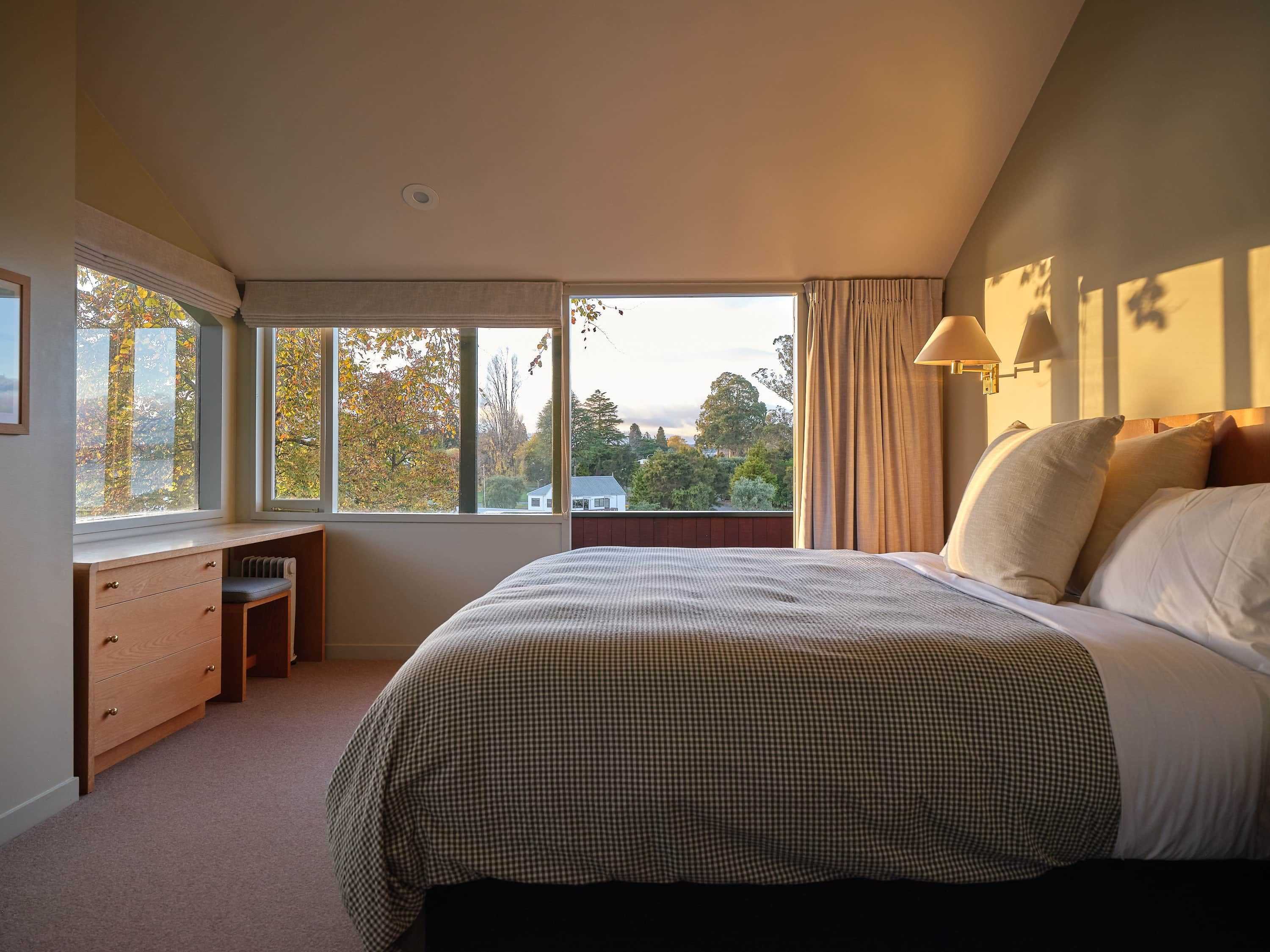 A bedroom with a large bed, a desk, and a window with curtains.