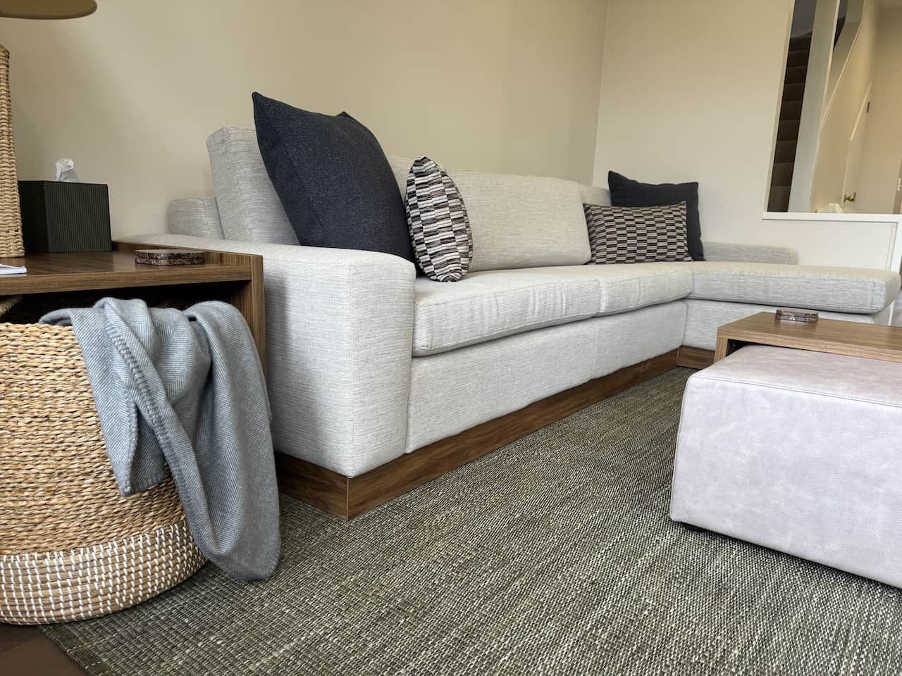 A sectional sofa with a wooden base, a woven basket, and a grey throw blanket.