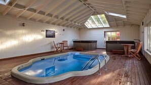 Una piscina interior con terraza de madera, un jacuzzi y zonas de estar.