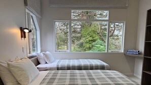 Un dormitorio con dos camas, una ventana con vistas a árboles y un estante con toallas dobladas.