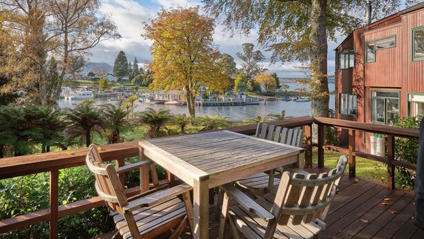 A wooden deck with a table and chairs overlooking a lake with boats and a dock. - Chalet 8 (Taupo)