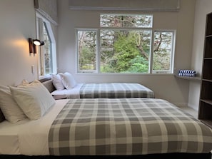 A bedroom with two beds, a window with a view of trees, and a shelf with folded towels.