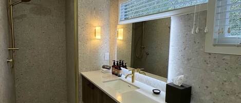 A modern bathroom with a walk-in shower, a large mirror, and a vanity with a towel rack.
