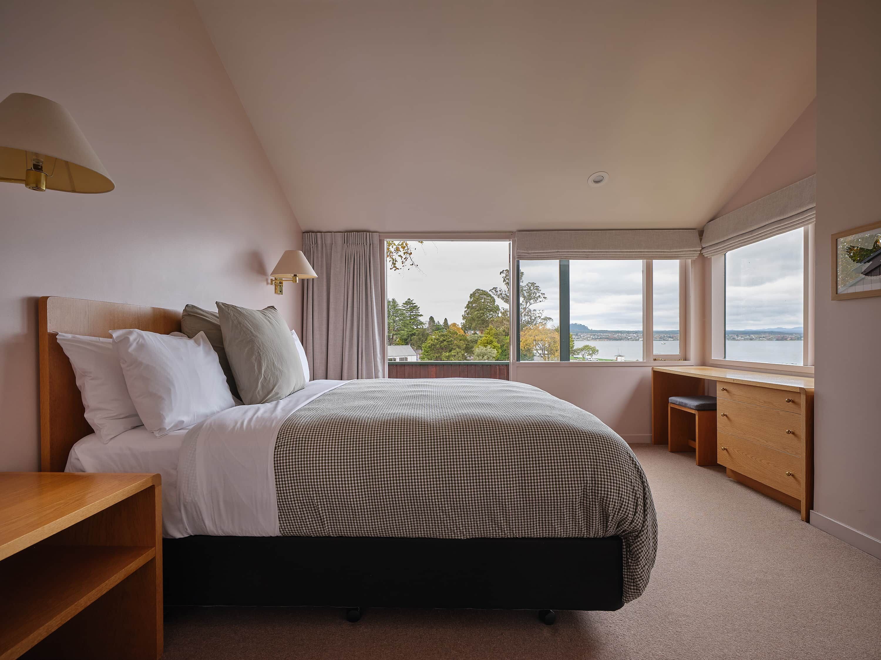 A bedroom with a bed, bedside tables, a desk, and a window with a view.