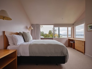 A bedroom with a bed, bedside tables, a desk, and a window with a view. - Chalet 5 @ The Retreat (Taupo)