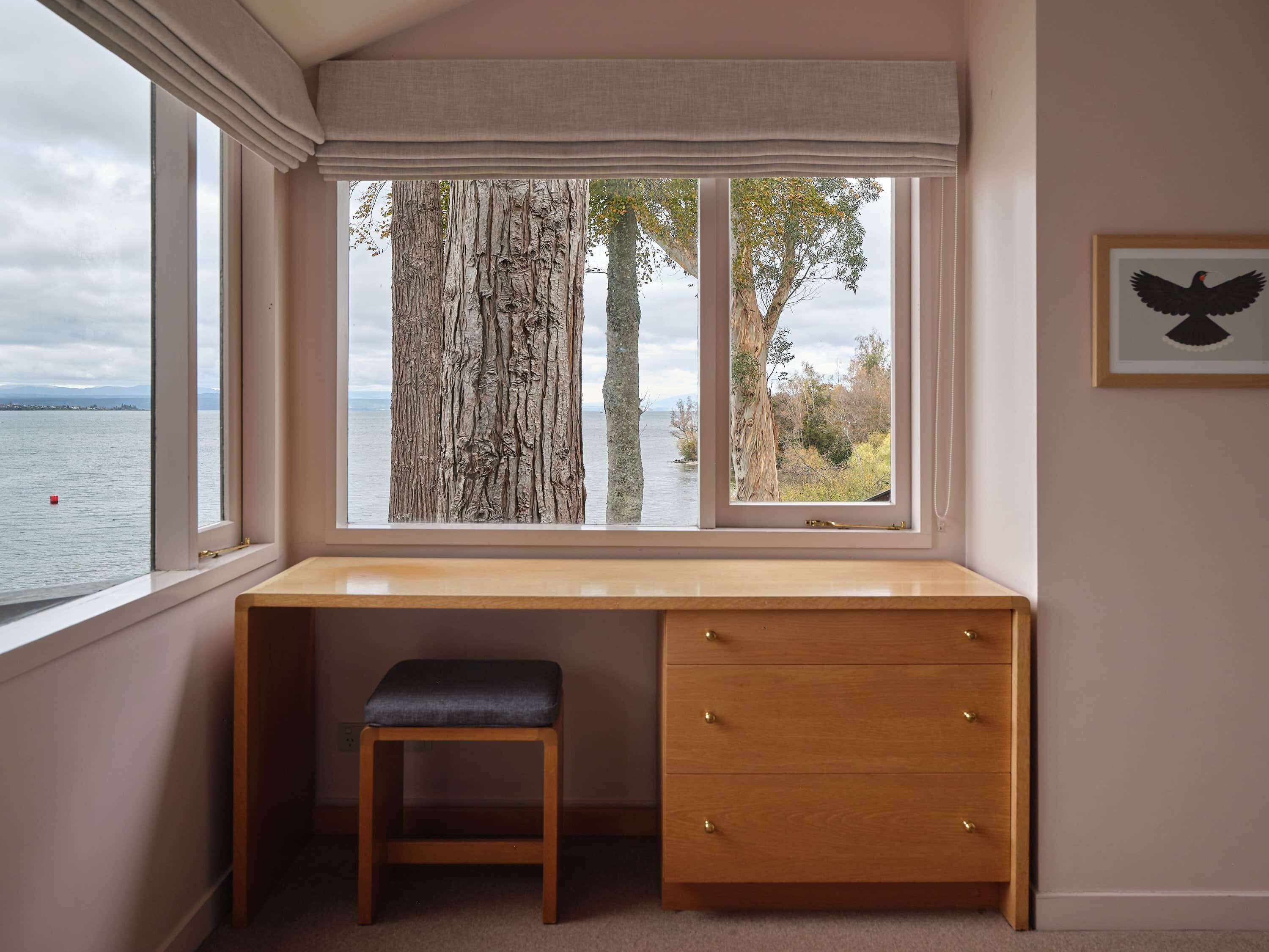 Ein Zimmer mit großem Fenster mit Blick auf ein Gewässer, einem Holztisch mit Schubladen und einer Bank.