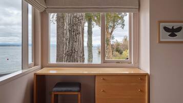 Ein Zimmer mit großem Fenster mit Blick auf ein Gewässer, einem Holztisch mit Schubladen und einer Bank.