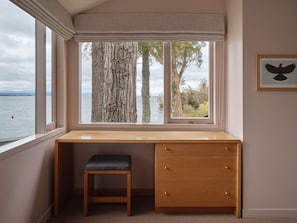 Una habitación con un ventanal grande que da a una masa de agua, un escritorio de madera con cajones y un banco.