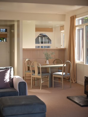 A cozy room with a dining table, chairs, a sofa, and a window with curtains. - Chalet 2 @ The Retreat (Taupo)