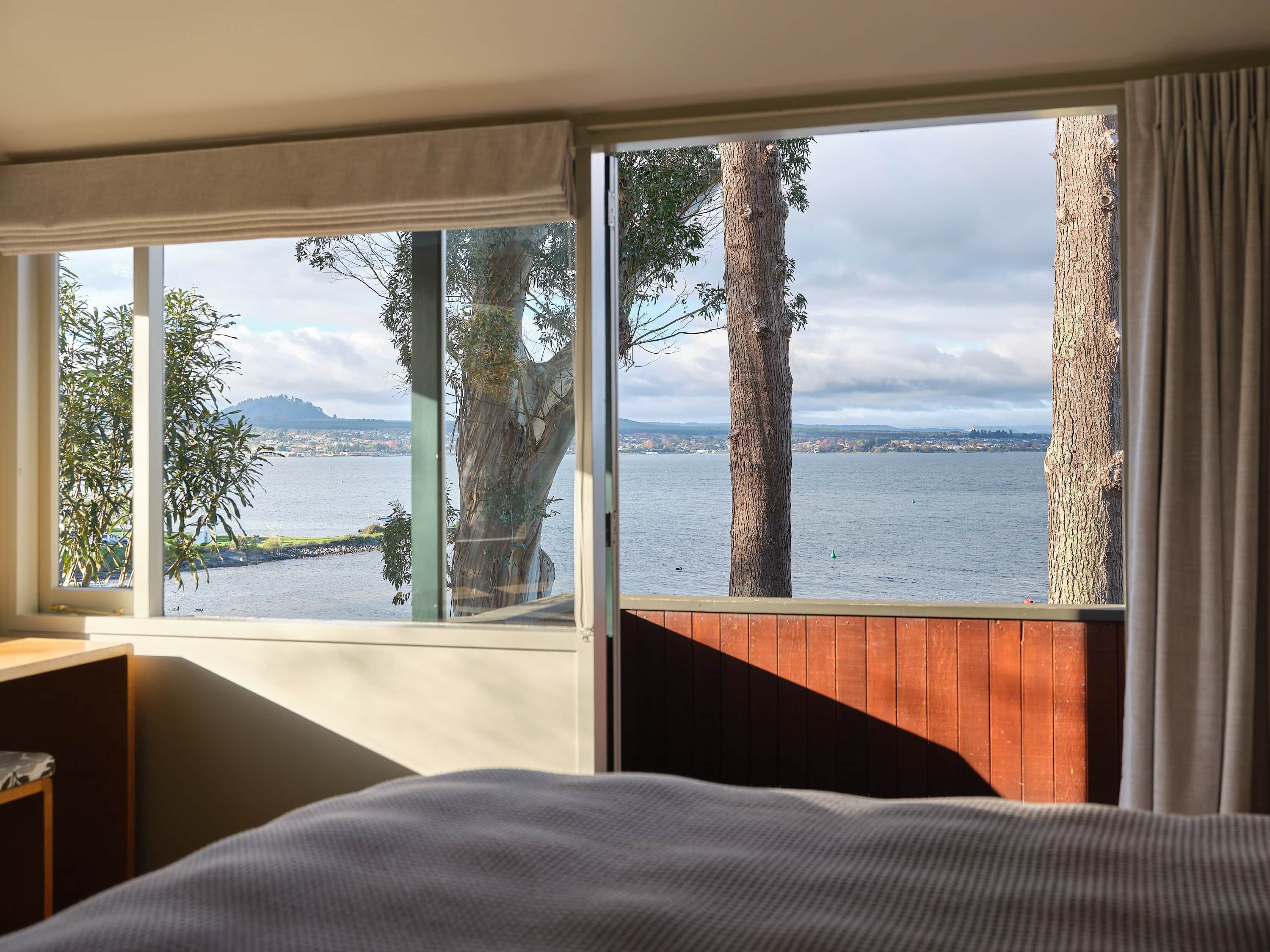 A room with a large window overlooking a body of water, a bed, and a wooden partition.