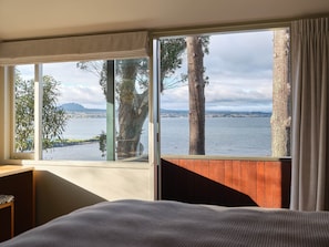 A room with a large window overlooking a body of water, a bed, and a wooden partition. - Chalet 2 @ The Retreat (Taupo)