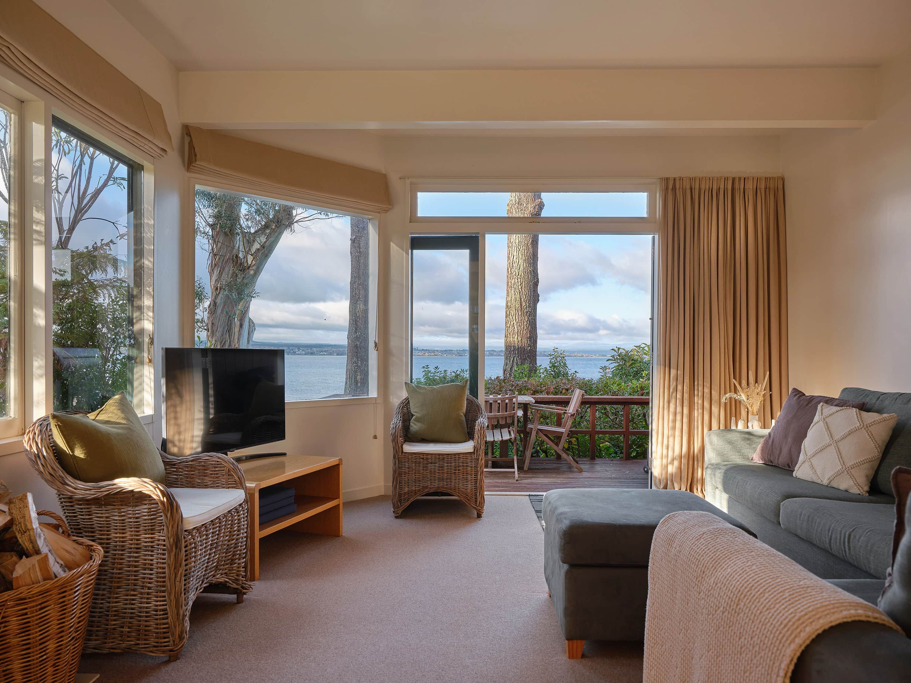 Un salon avec un téléviseur, des meubles en osier, un canapé gris et une vue sur la mer.