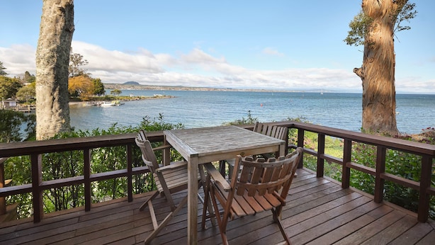 Une terrasse en bois avec une table et des chaises, donnant sur une étendue d’eau où se trouvent des bateaux et, au loin, une côte.