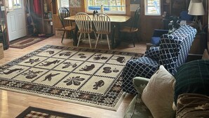 A rustic cabin interior with a dining area, a large rug, and a cozy seating area. - Escape to Green Lake (Ellsworth)