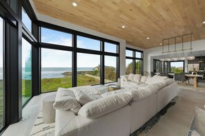 Una sala de estar moderna con un sofá seccional blanco grande, un comedor y una cocina con iluminación colgante.