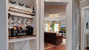 A modern kitchen with wine bottles, coffee machines, and kitchenware on shelves.