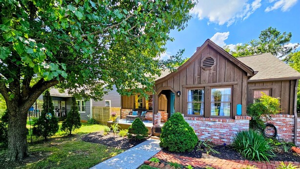 A residential house with a brick and wood exterior, a front porch, and a well-maintained garden with a pathway leading to the entrance.