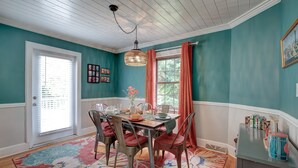 A dining room with a table set for four, a chandelier, and a window with curtains.