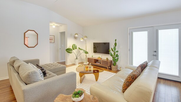 A modern living room with a sofa, armchair, coffee table, and a TV. There are plants and a wooden cabinet. - 3 Mi to Escambia Bay: Home w/ Deck & Private Yard! (Milton)