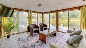 Una habitación con un sofá, dos sillones, una mesita de centro, un televisor y ventanas amplias con vista a un cuerpo de agua.
