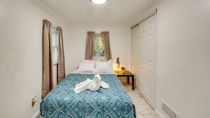 Un dormitorio con cama, cortinas, una mesita de noche con lámpara y una puerta.