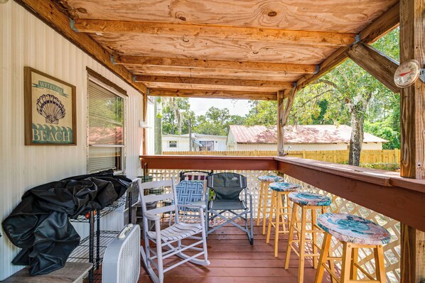 Ein überdachter Balkon mit Grill, Klappstühlen und einer Holzterrasse.