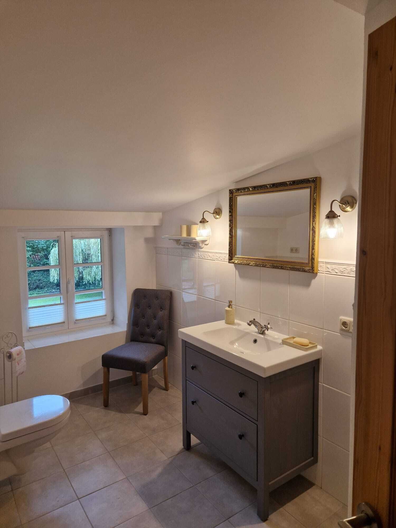 A bathroom with a vanity, a mirror, a chair, and a toilet.