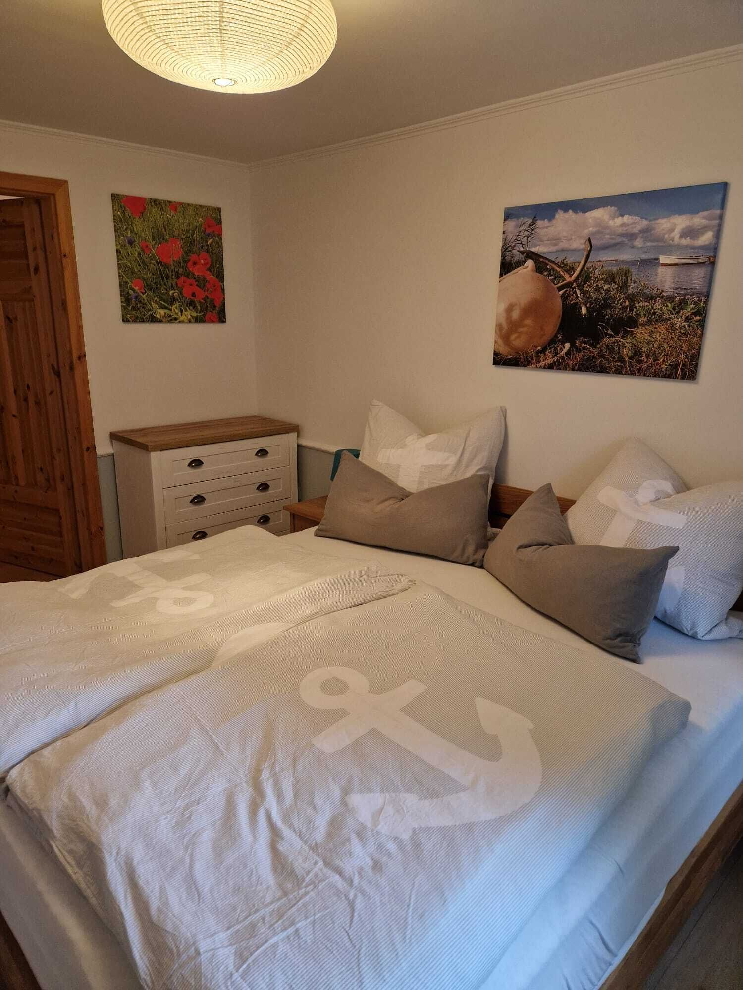 A bedroom with a bed, a nightstand, a dresser, and two wall-mounted paintings.