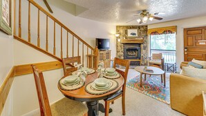 A dining area with a wooden table set for four, a staircase, a living room with a sofa, and a fireplace.