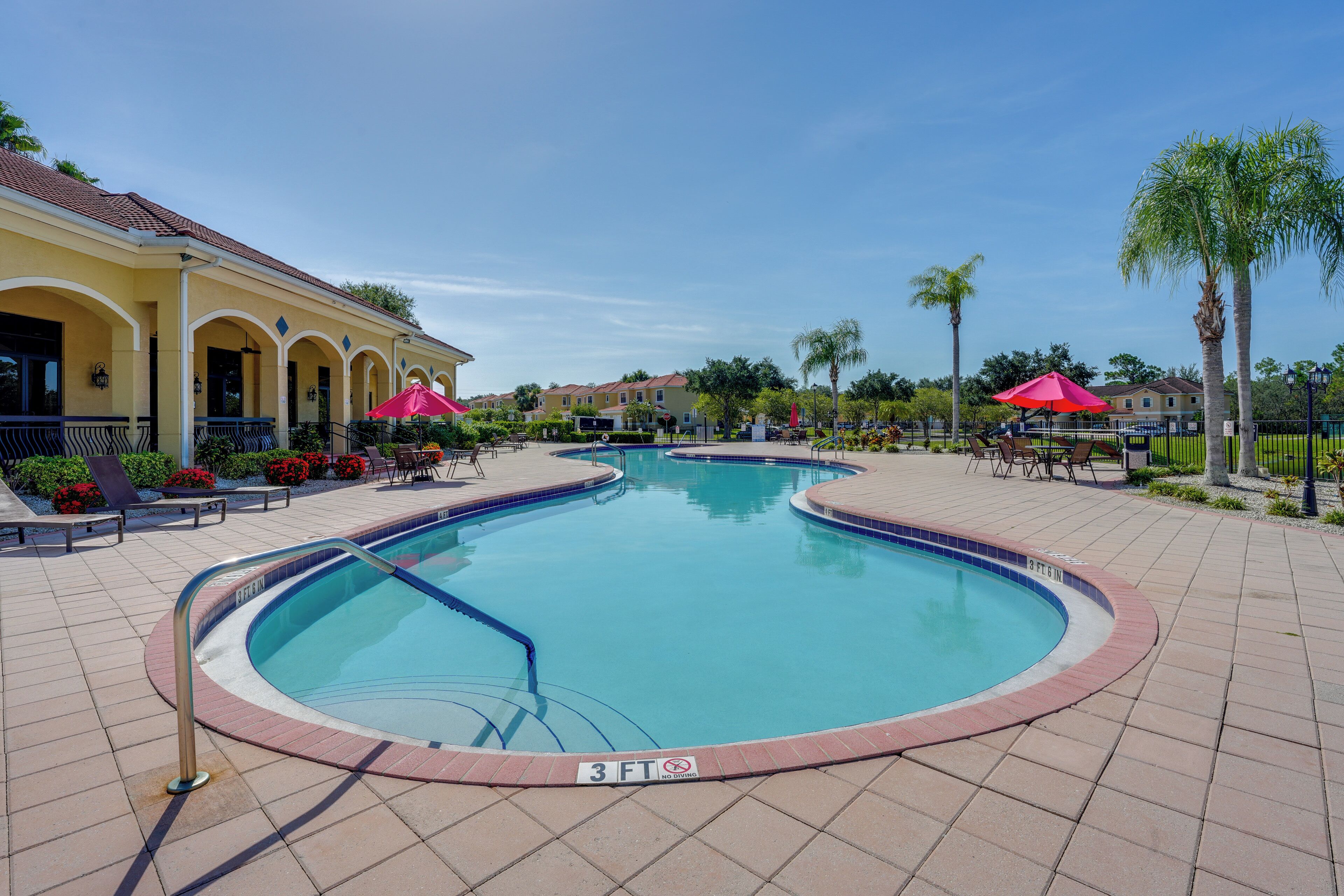 A swimming pool with a 3 ft depth marker, surrounded by a tiled deck with outdoor seating and palm trees.