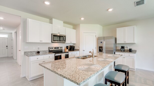 Una cucina moderna con mobili bianchi, piani di lavoro in granito, un'isola centrale con sgabelli ed elettrodomestici in acciaio inossidabile.