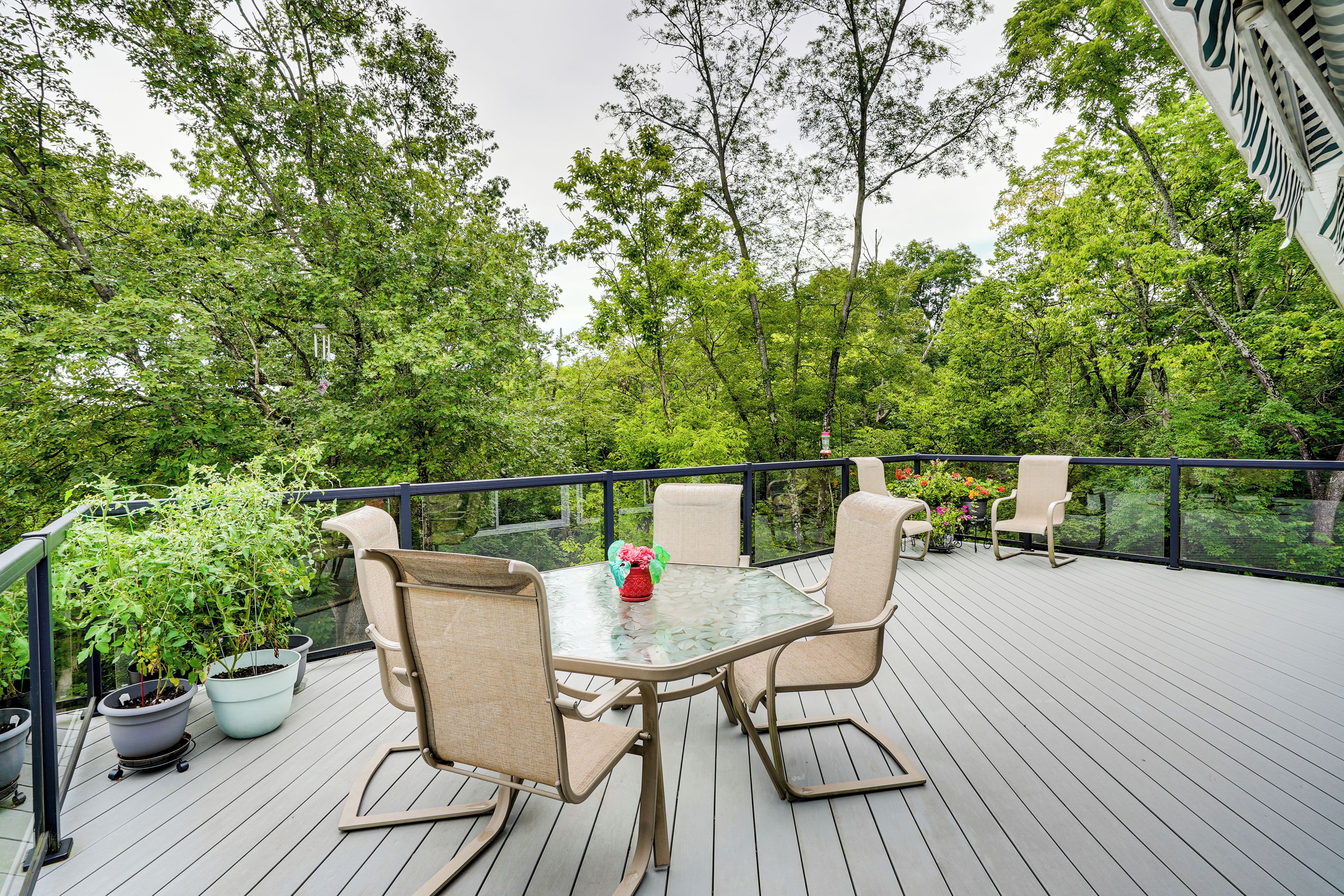 Une terrasse dotée d’une table en verre et de quatre chaises, entourée de plantes en pot et d’une rambarde.