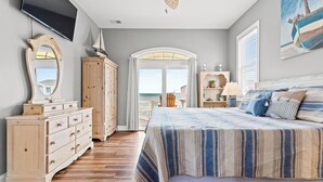 Une chambre avec un grand lit, une commode en bois et un téléviseur fixé au mur.