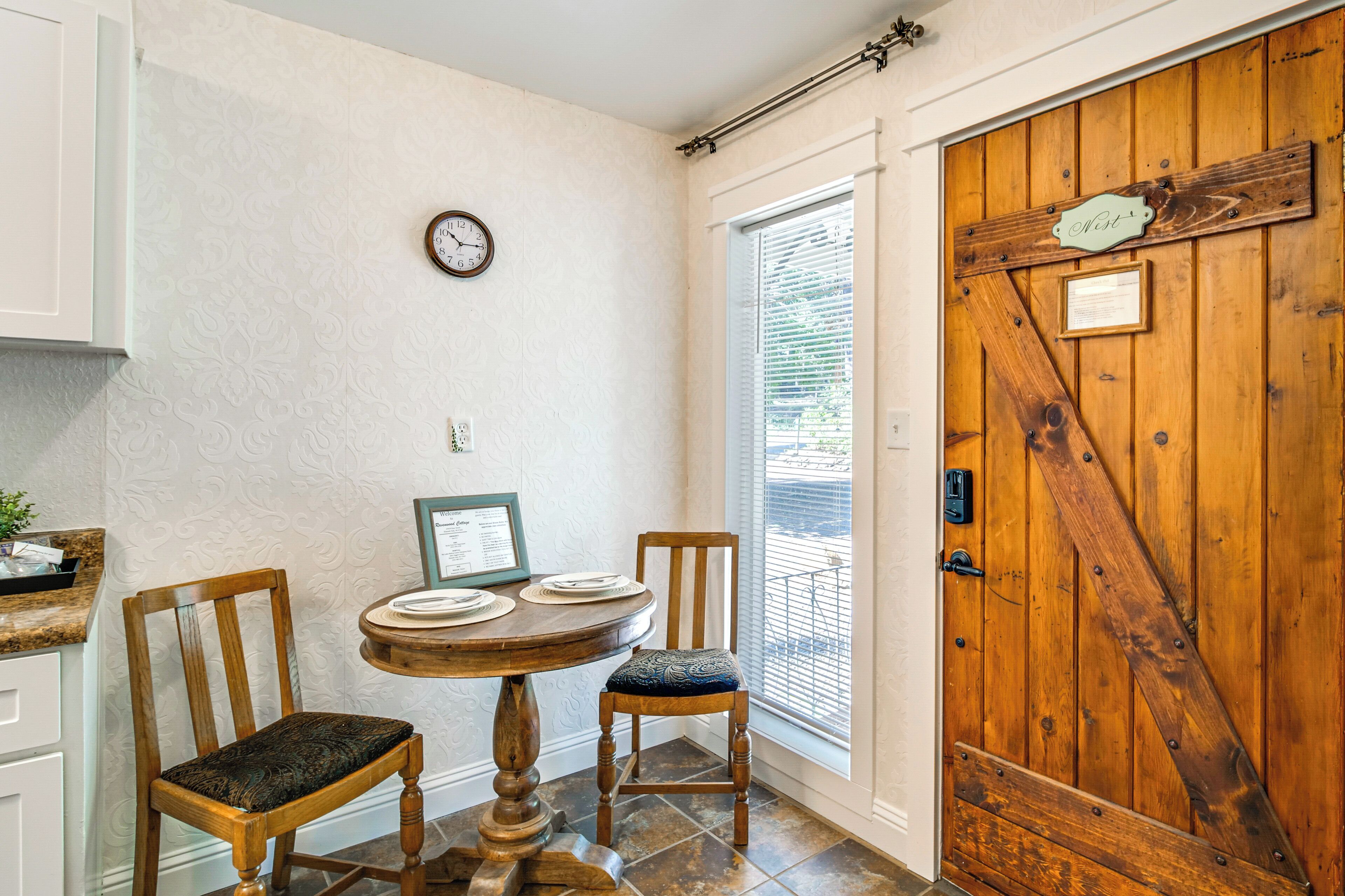 Una puerta de madera con diseño rústico, una mesa de comedor con sillas, un reloj en la pared y una ventana con persianas.