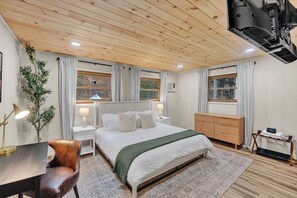 Ein Schlafzimmer mit Holzbalkendecke, einem Bett mit weißer Bettwäsche, einem Schreibtisch mit Stuhl und einer Kommode.