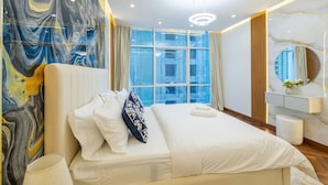 Une chambre d’hôtel moderne dotée d’un grand lit, d’un mur en marbre, d’une grande fenêtre et d’une salle de bain avec un miroir et un lavabo.