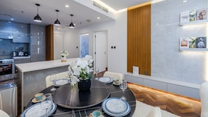 Un espace repas moderne avec une table ronde dressée pour quatre personnes, une cuisine en arrière-plan et un mur d’accent en bois.