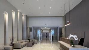 Un hall d’entrée moderne avec un sol en marbre, des canapés, un comptoir de réception et un ascenseur en verre.